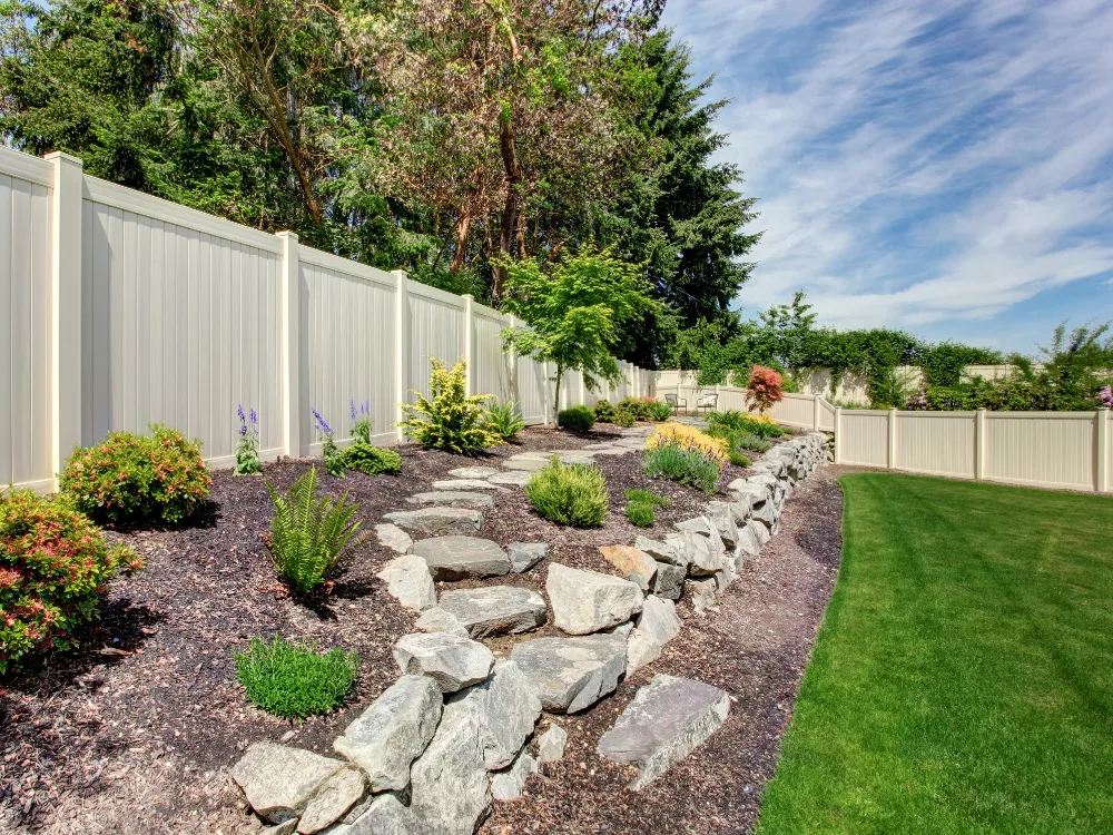 A stone-edged terraced garden bed with a stepping-stone path against a solid privacy fence - Fencing and Landscaping Experts, terraced garden landscaping contractors in Sydney